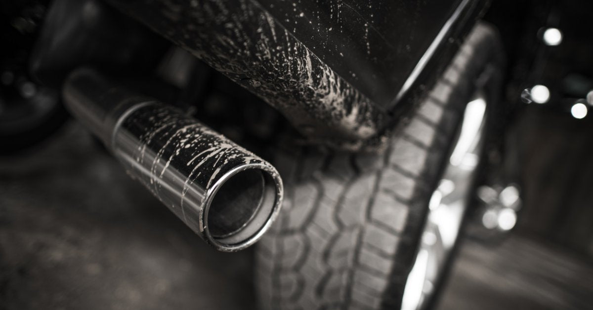 A chrome exhaust tip with road grime and water spots on it, positioned beside the rear tire and lower body panel of a truck.