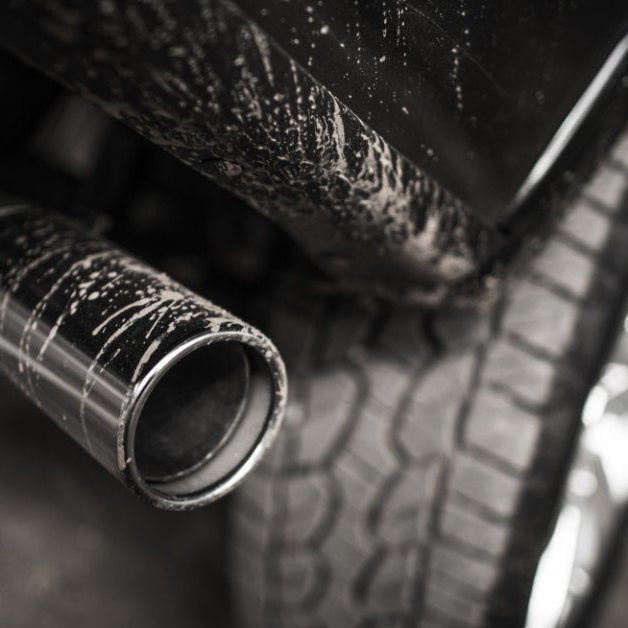 A chrome exhaust tip with road grime and water spots on it, positioned beside the rear tire and lower body panel of a truck.
