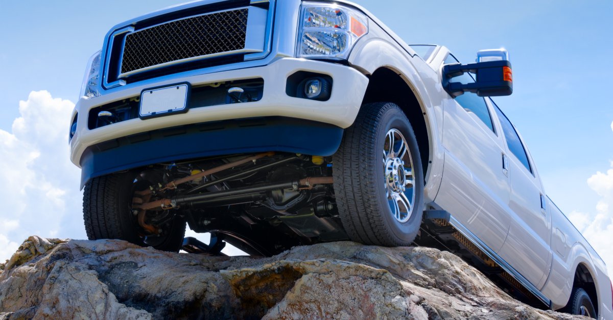 A white diesel pickup truck climbing over rocky terrain under a clear blue sky.
