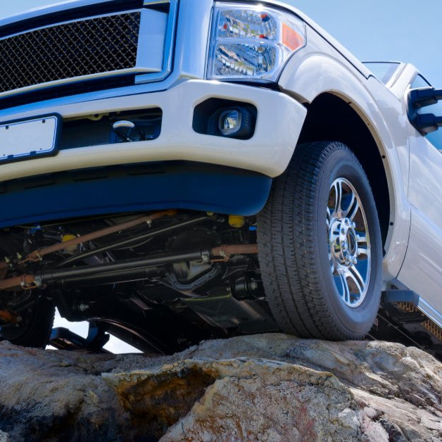 A white diesel pickup truck climbing over rocky terrain under a clear blue sky.